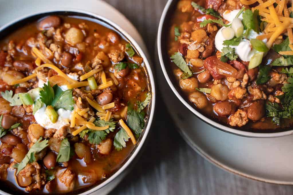 2 bowls of turkey chili for two garnished with cilantro, sour cream and cheddar cheese as garnish
