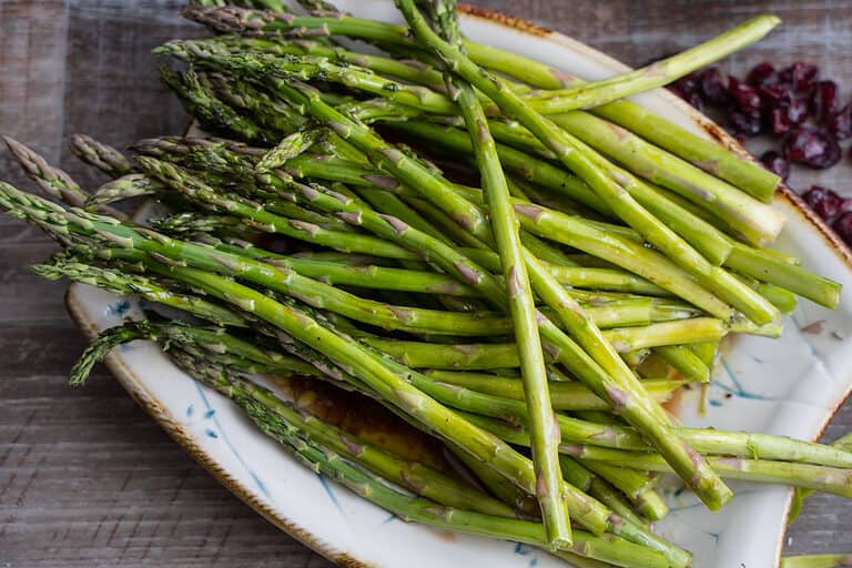 Roasted Asparagus on a baking sheeting being moved with tongs to a serving platter