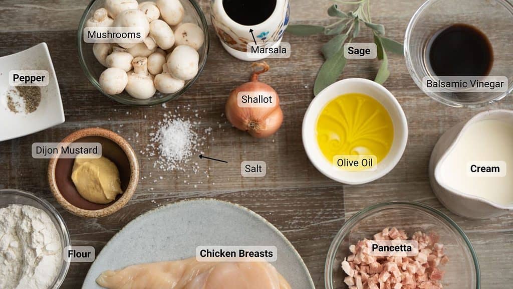 Ingredients to make Chicken Marsala on a wood table, each ingredient is labeled.