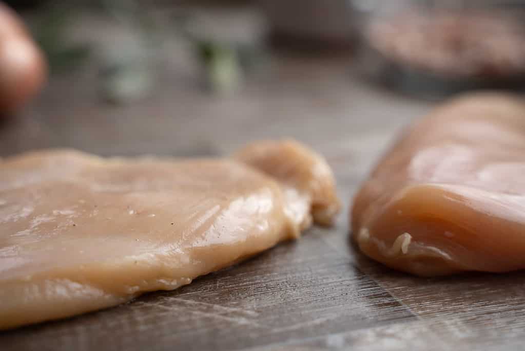 Chicken breasts pounded to ½ inch thickness next to  chicken breast yet to be preparedd