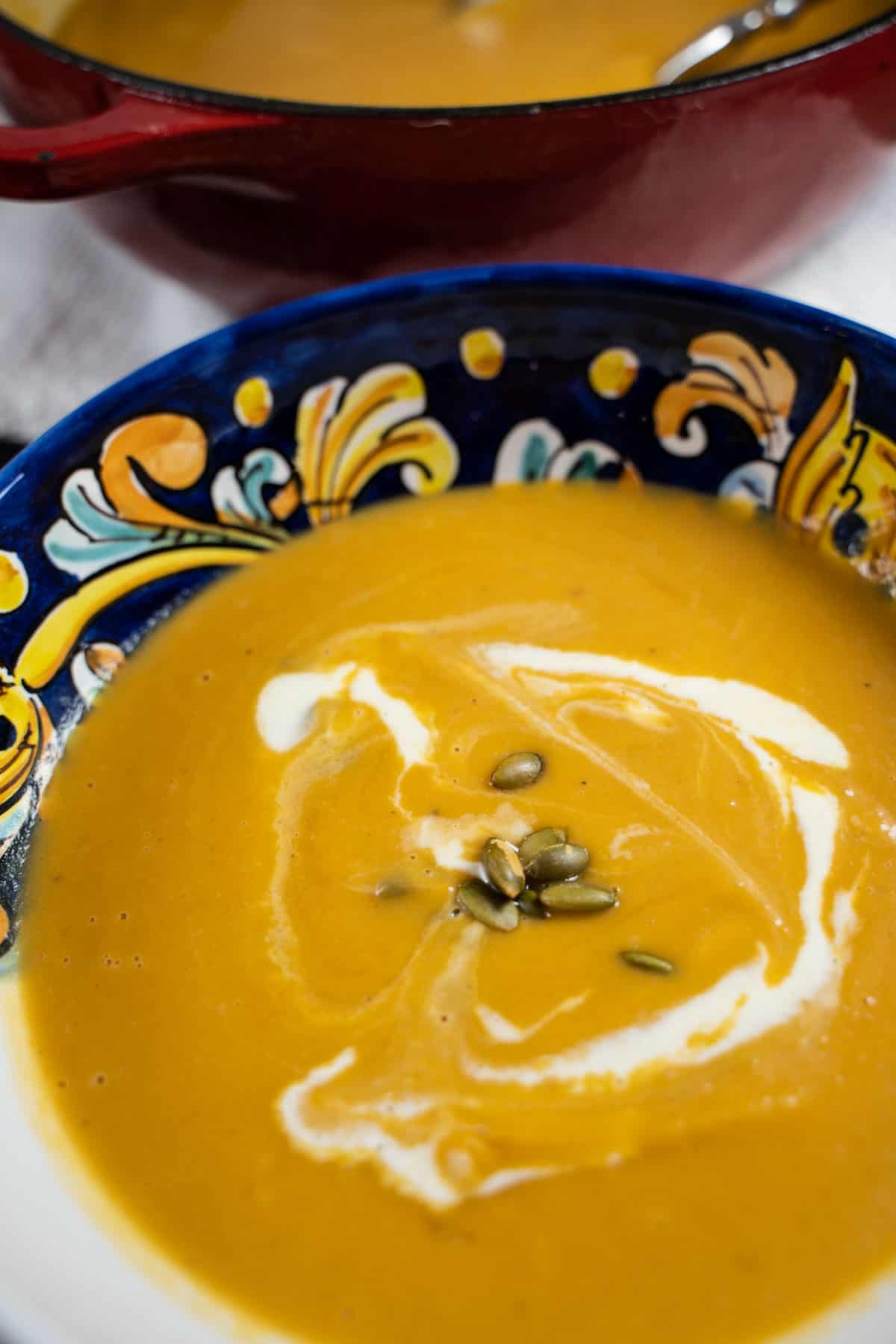 Roasted Butternut Squash, pear and ginger soup pureed in a Italian hand painted bowl on a wood table.