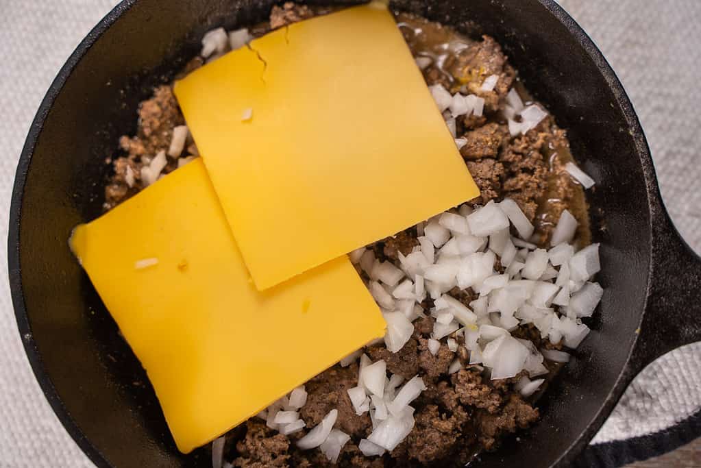 simmered ground beef topped with onions and american cheese in a skillet