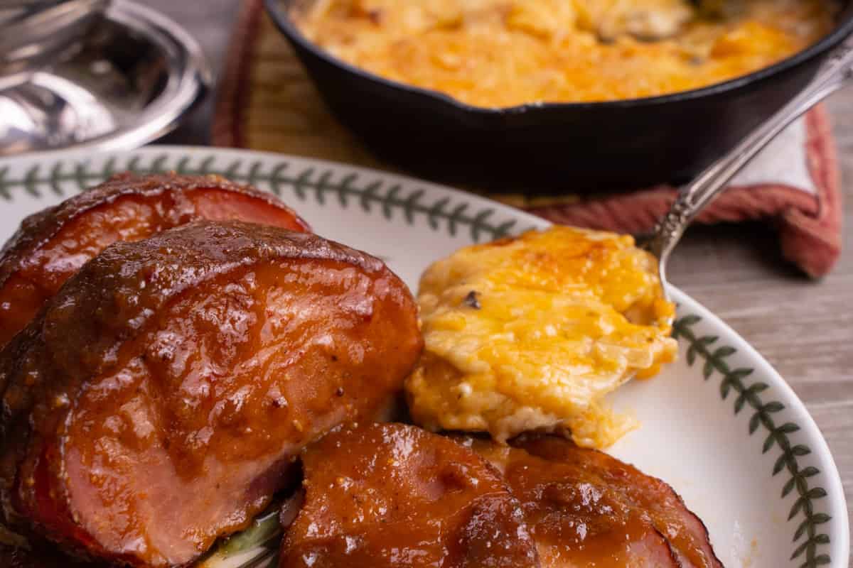 small glazed ham on platter with scalloped potatoes