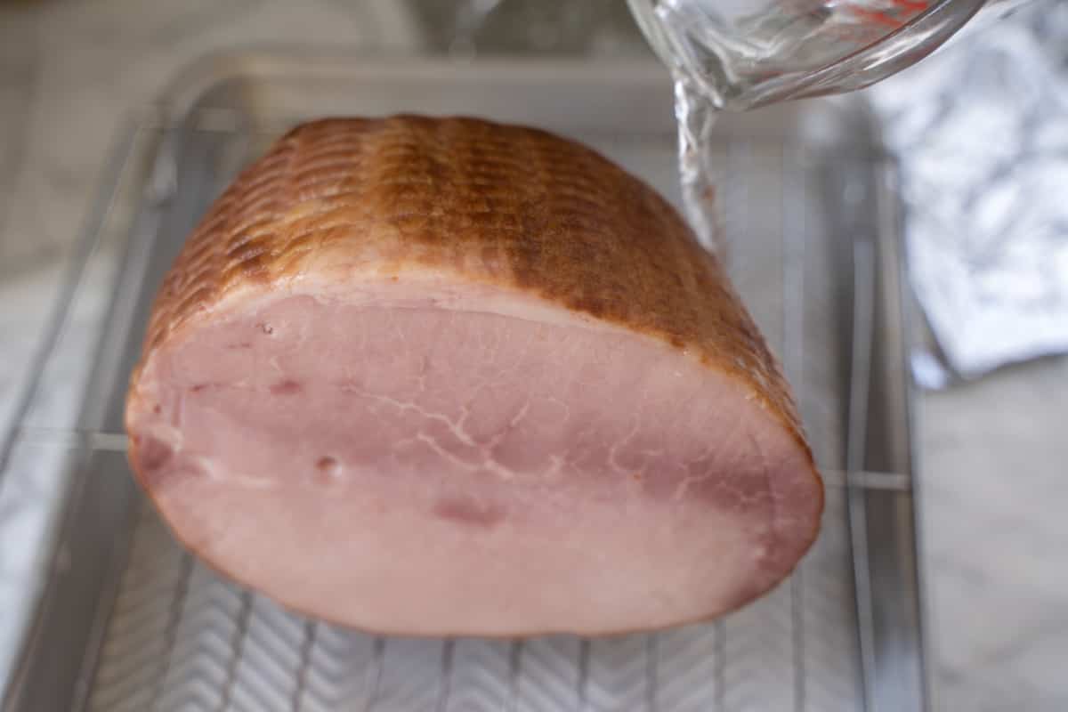 water being added to baking sheet with small ham.