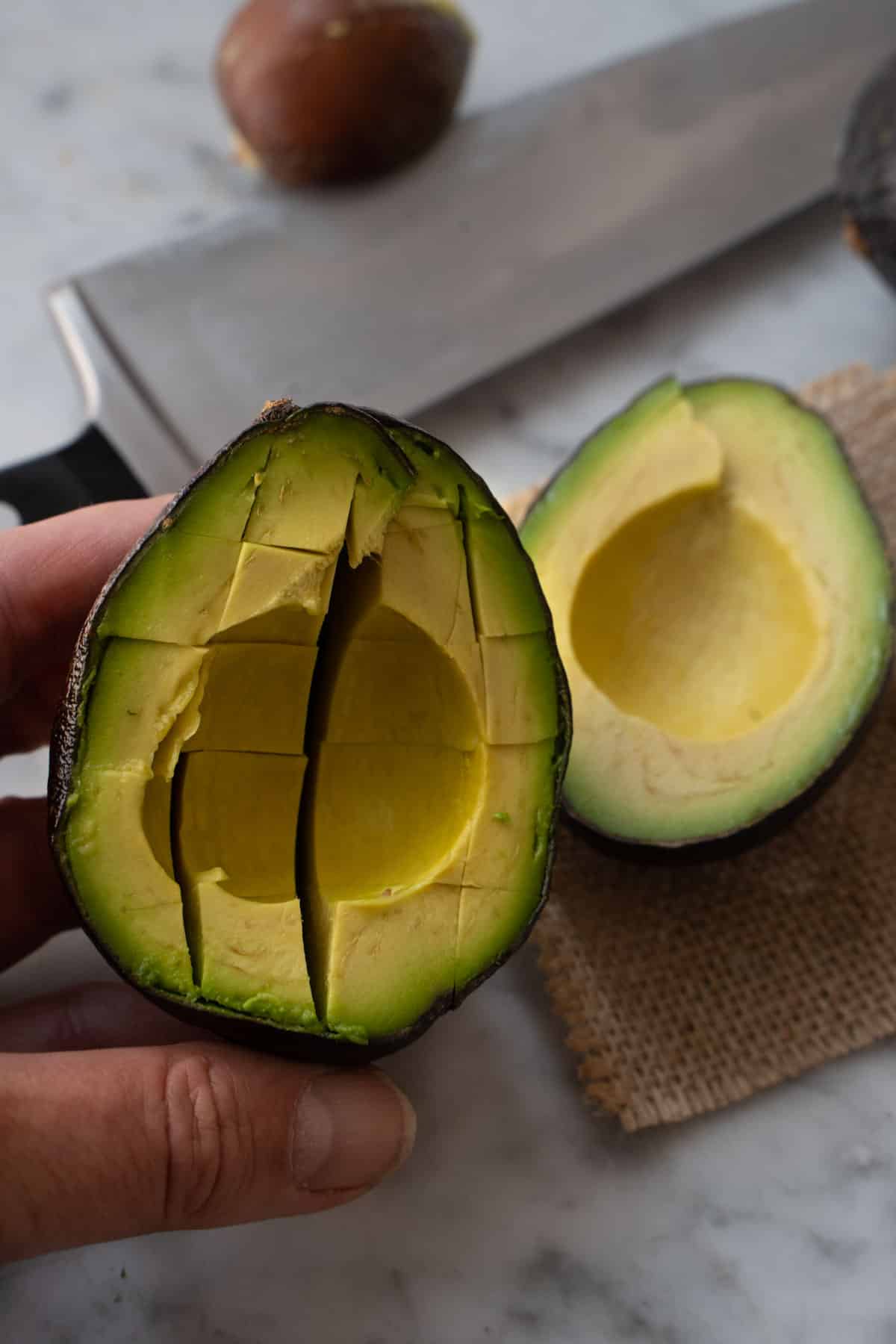 left hand holding an avocado half with a cross hatch pattern