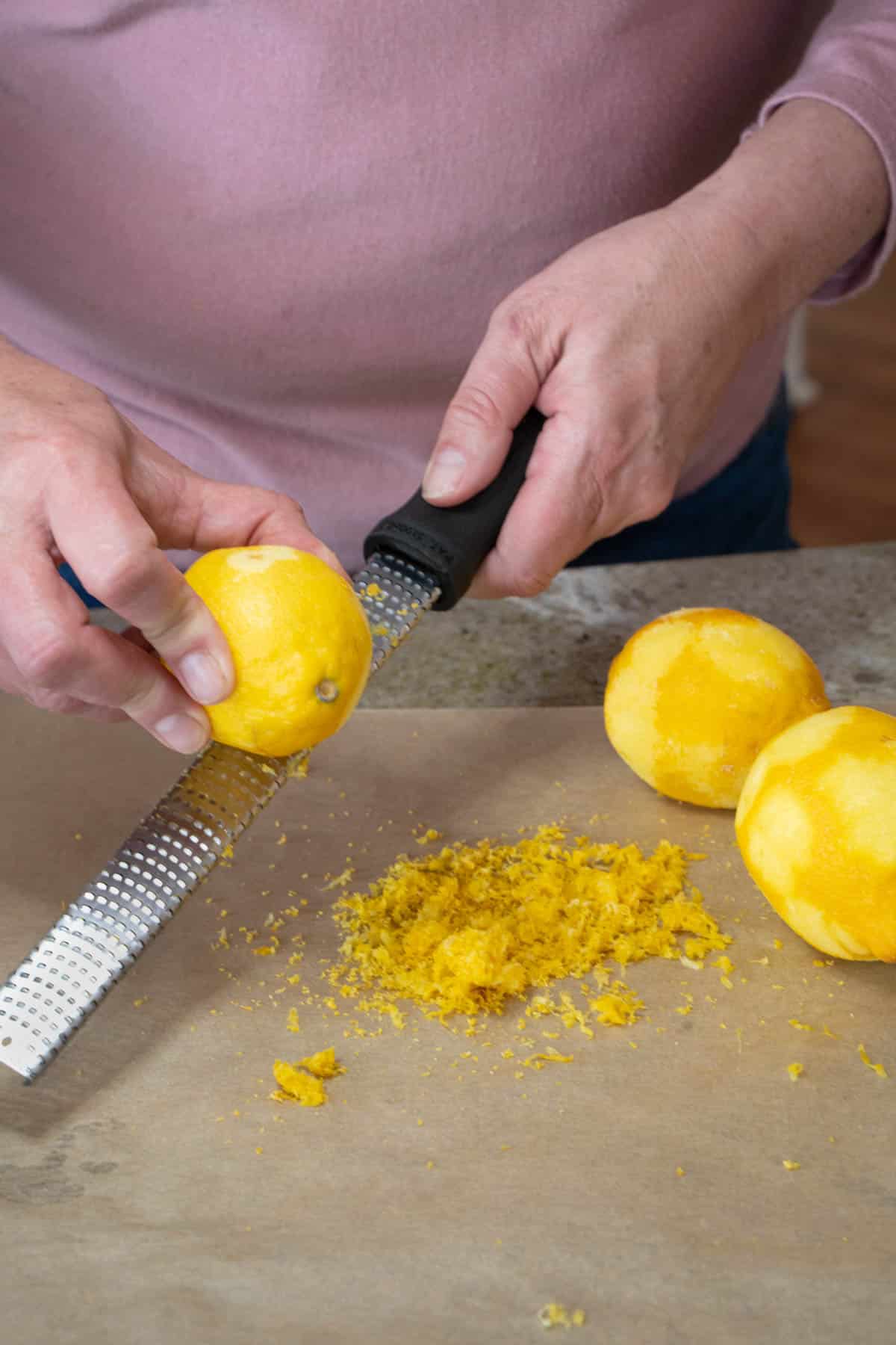 using 2 hands and a zester to zest a whole lemon onto parchment paper