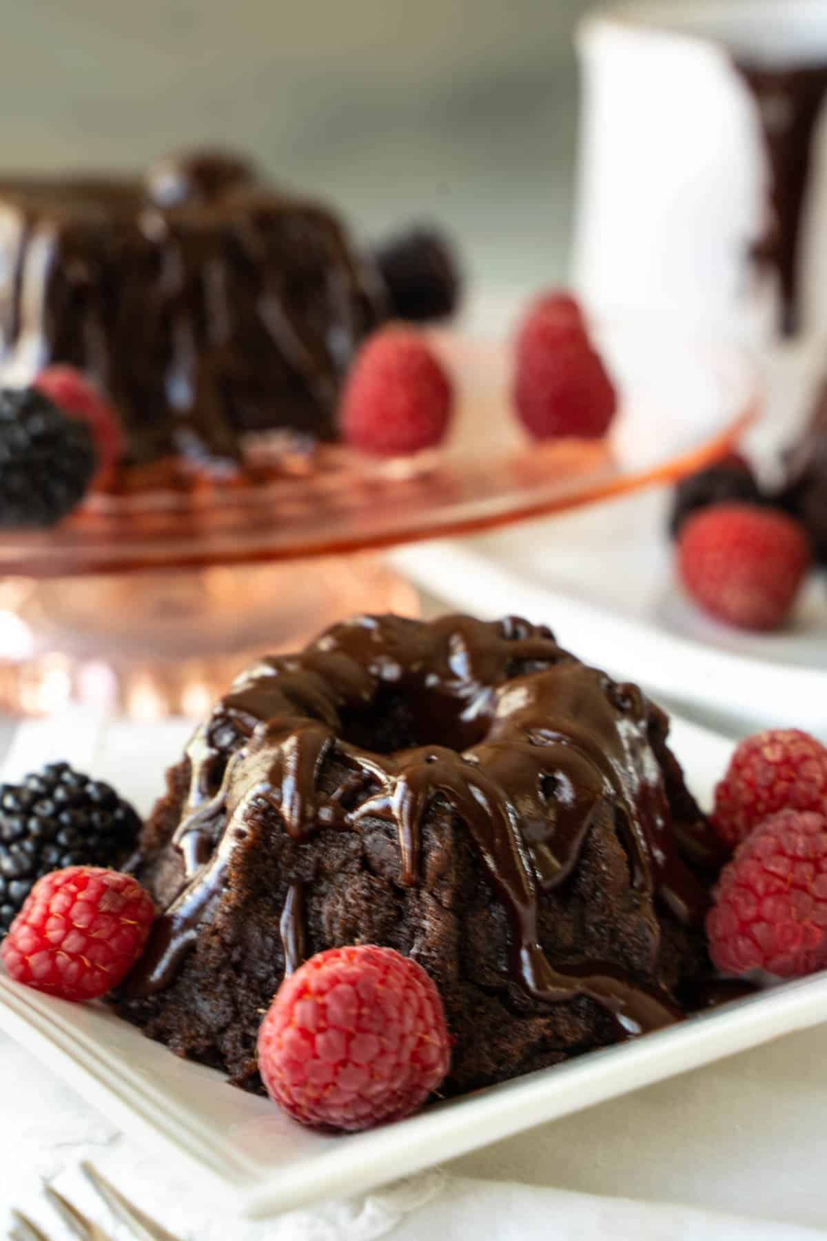 mini chocolate bundt cakes on individual plates and a cake plate garnished with raspberries and blackberries.