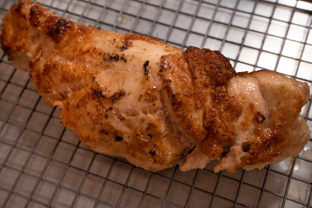 pork tenderloin after being seared resting on a wire rack inserted into a baking sheet