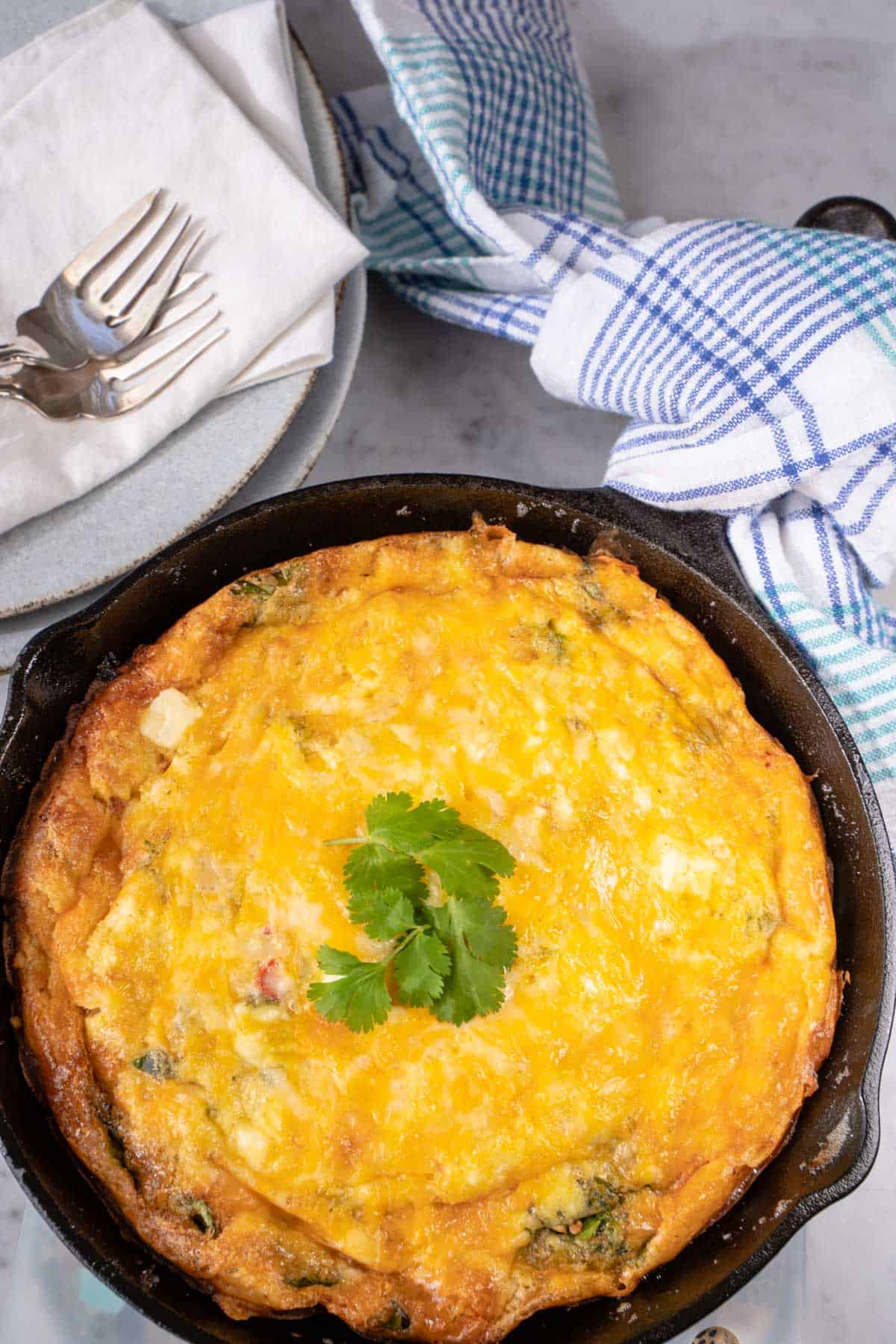 Frittata for two in a cast iron skillet with 2 plates ,forks and napkins resting next to the frittata