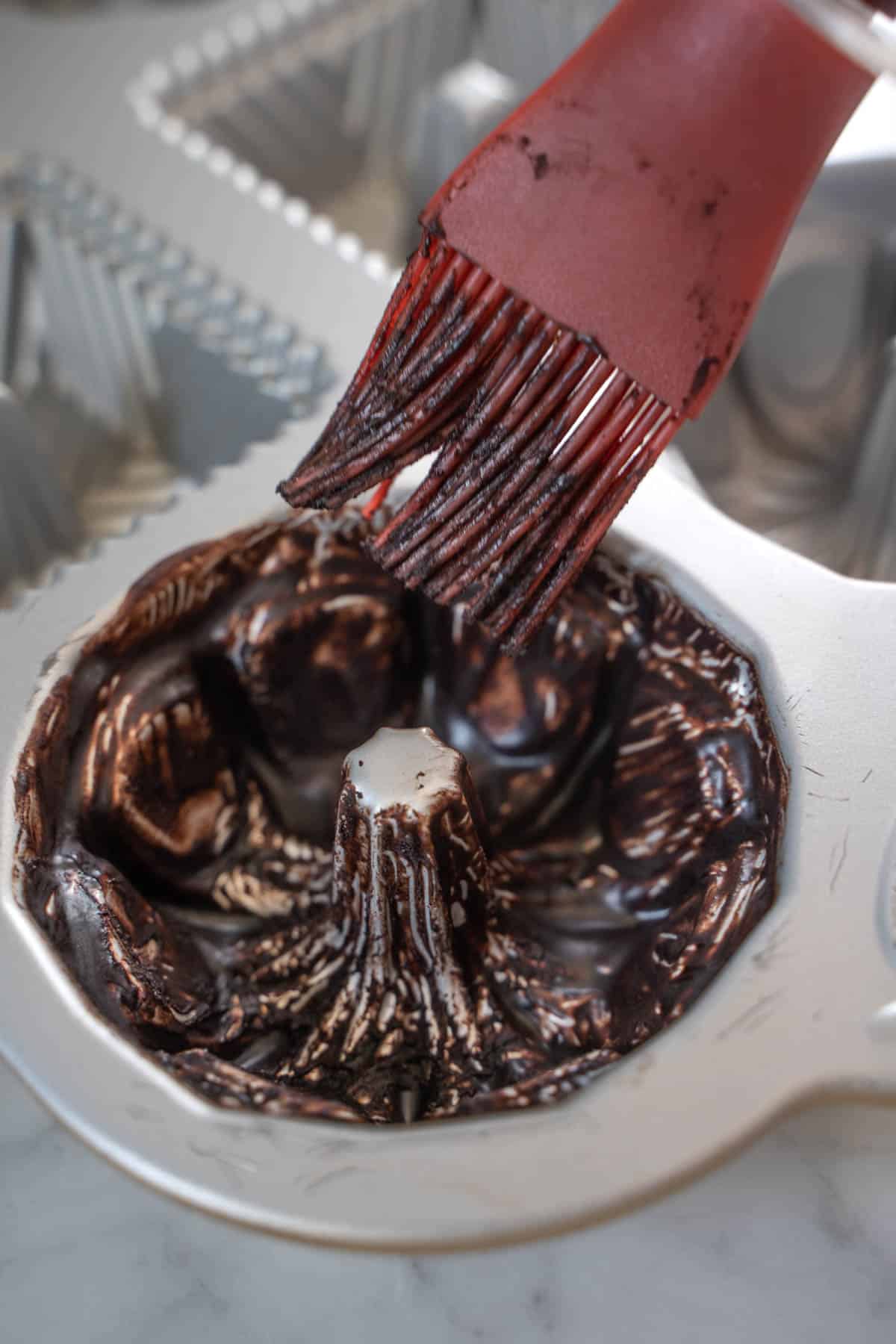using a pastry brush to prepare bundt pan with a cocoa powder and melted butter paste