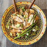 Sesame noodles topped with sliced chicken, diced cucumber and scallions and asparagus tips in a past bowl