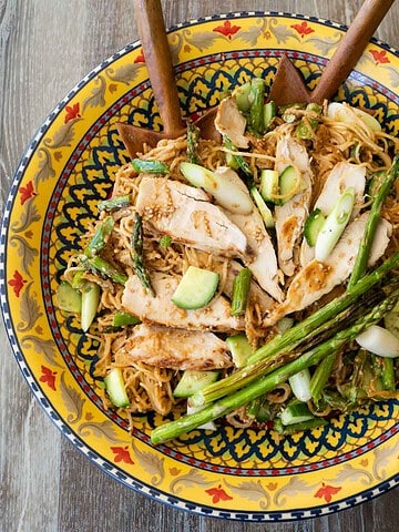 Sesame noodles topped with sliced chicken, diced cucumber and scallions and asparagus tips in a past bowl
