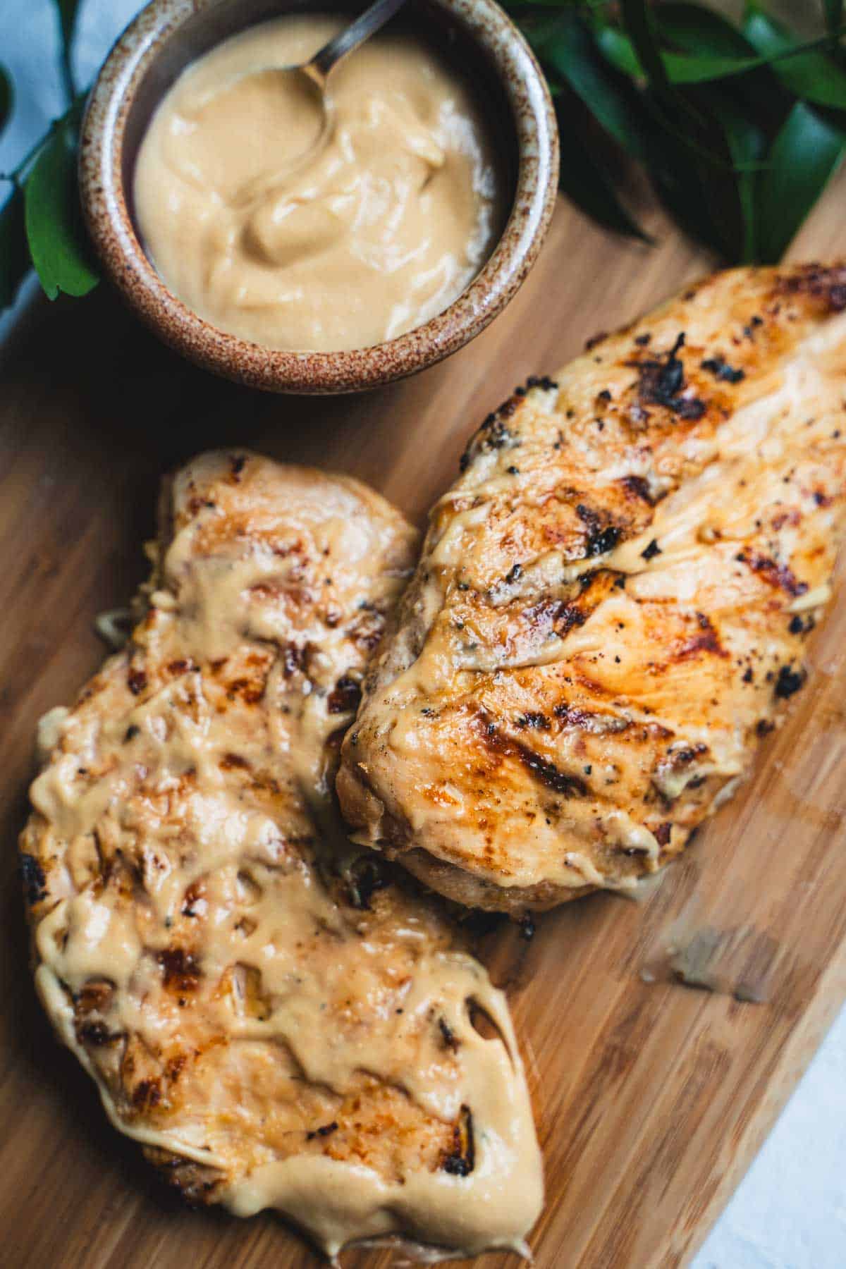 Mayo marinated chicken grilled chicken breasts on wooden cutting board with cup of mayo marinade