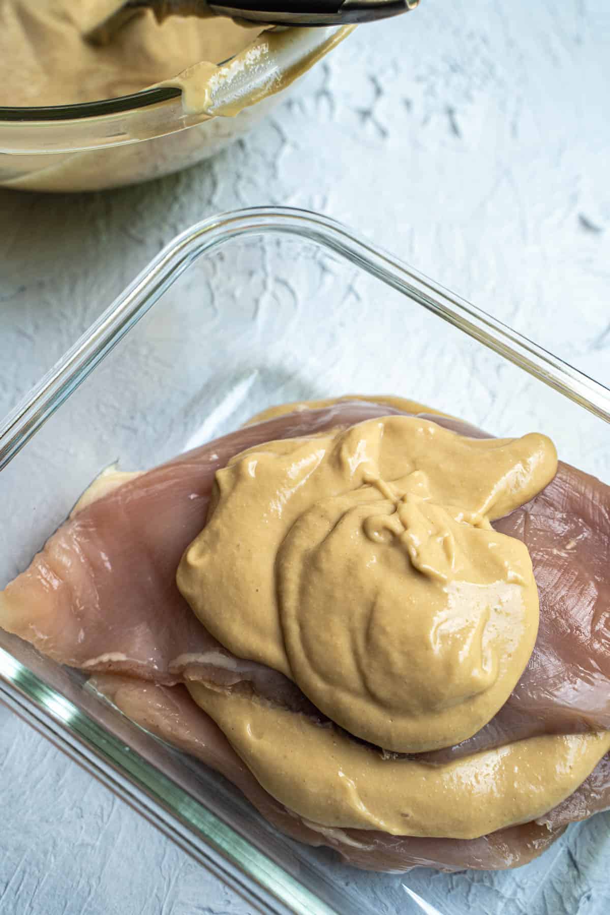 mayo marinade poured over chicken in a glass container