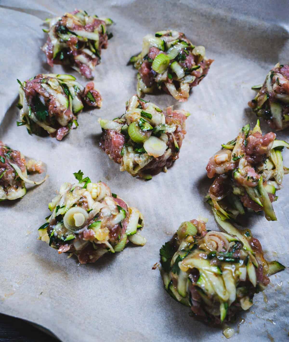 Meatballs in a spherical shape on a parchment paper lined sheet pan.