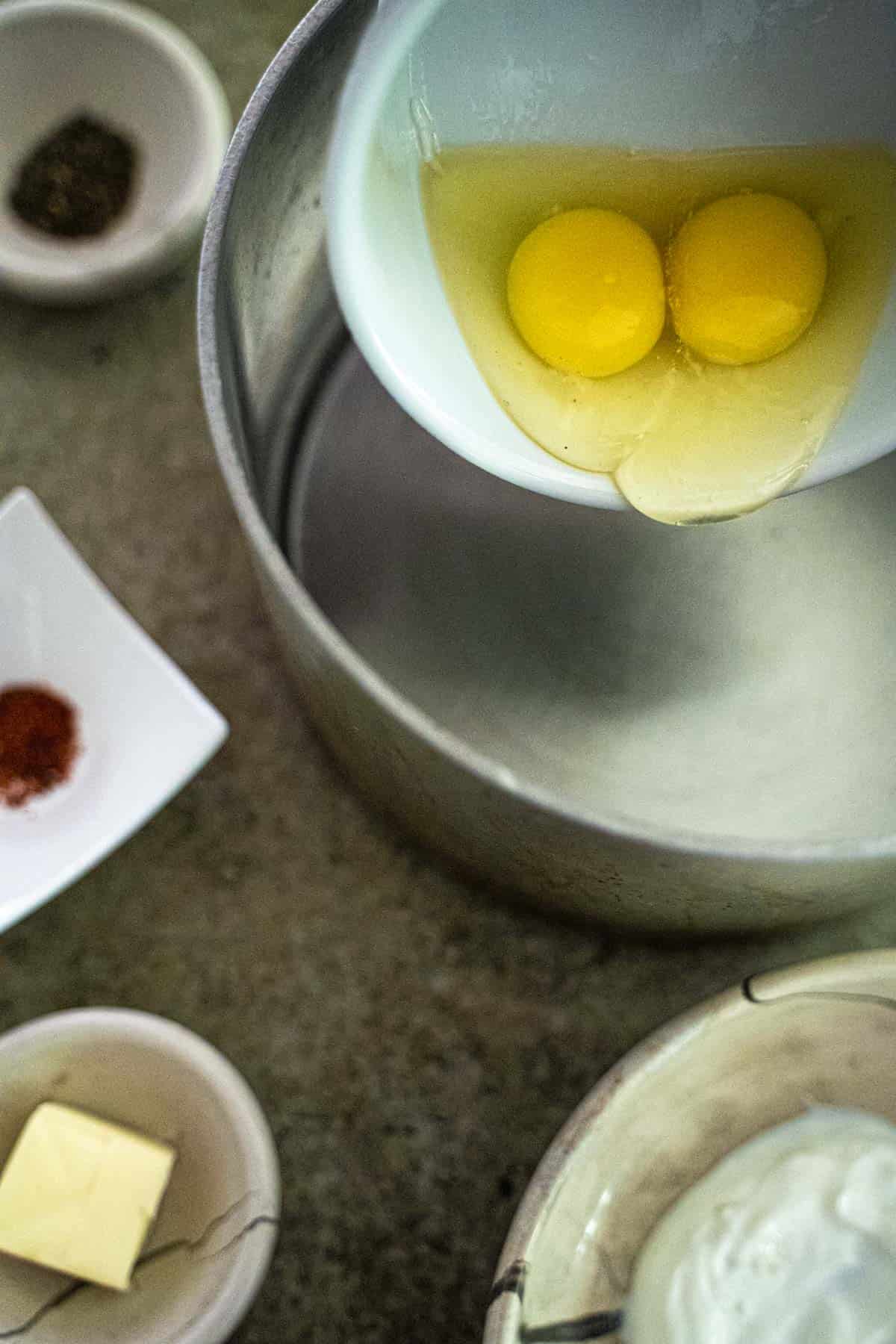 two eggs in small bowl over boiling water