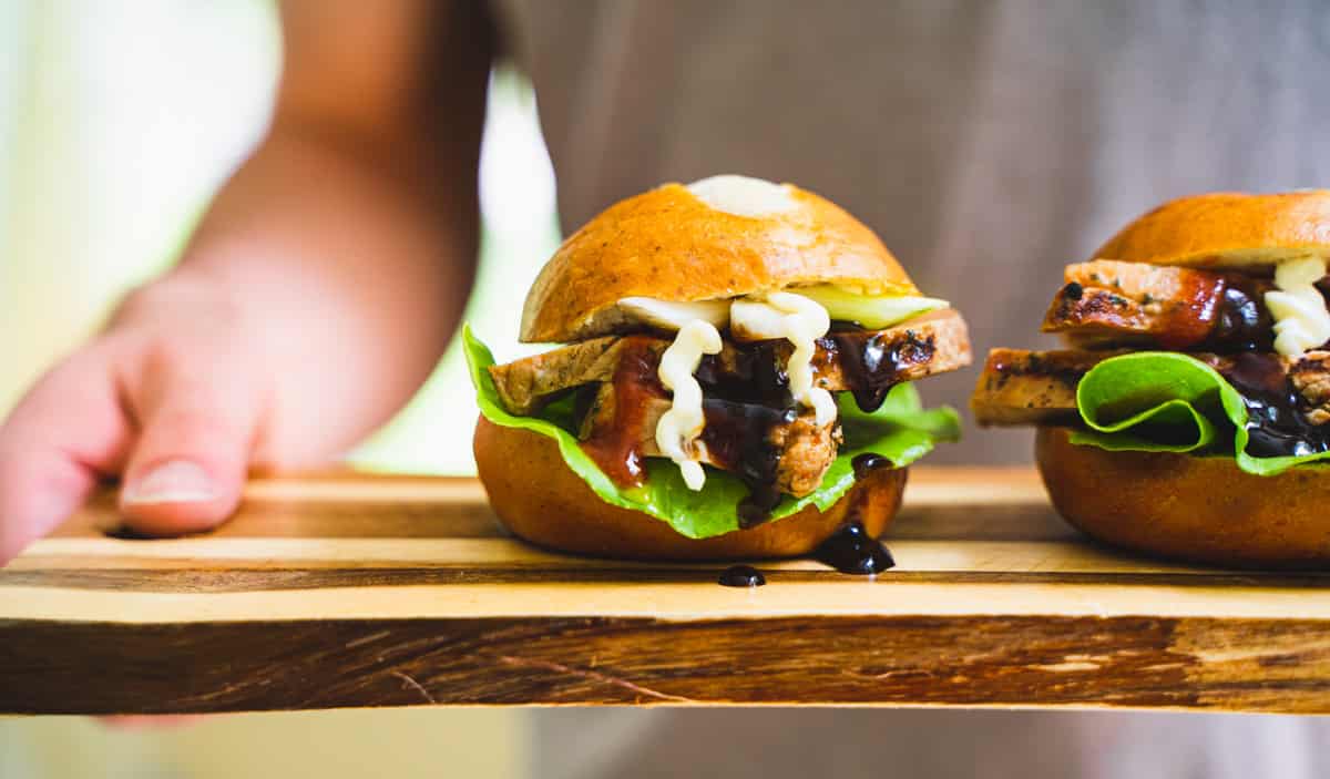 Pork Slider of sliced pork topped with miso mayo and hot sauce on a cutting board held by a person
