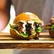 Pork Slider of sliced pork topped with miso mayo and hot sauce on a cutting board held by a person