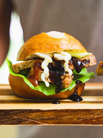 Pork Slider of sliced pork topped with miso mayo and hot sauce on a cutting board held by a person
