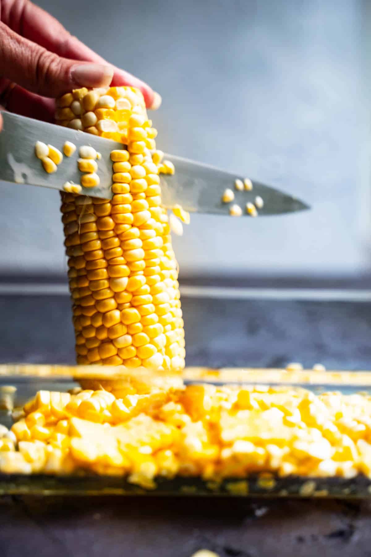 cob of corn upright inside a bowl with a sharp knife slicing down along sides