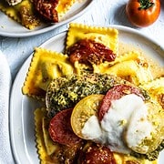 Baked pesto chicken breasts on a bed of ravioli with tomatoes and melted mozzarella