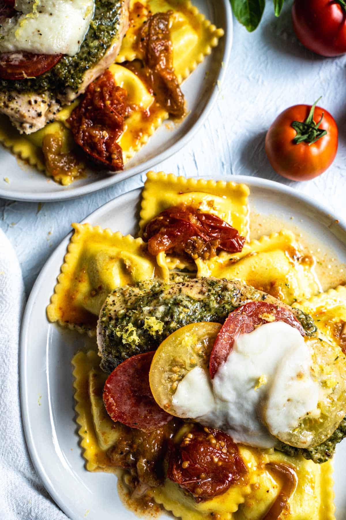 Baked pesto chicken breasts on a bed of ravioli with tomatoes and melted mozzeralla
