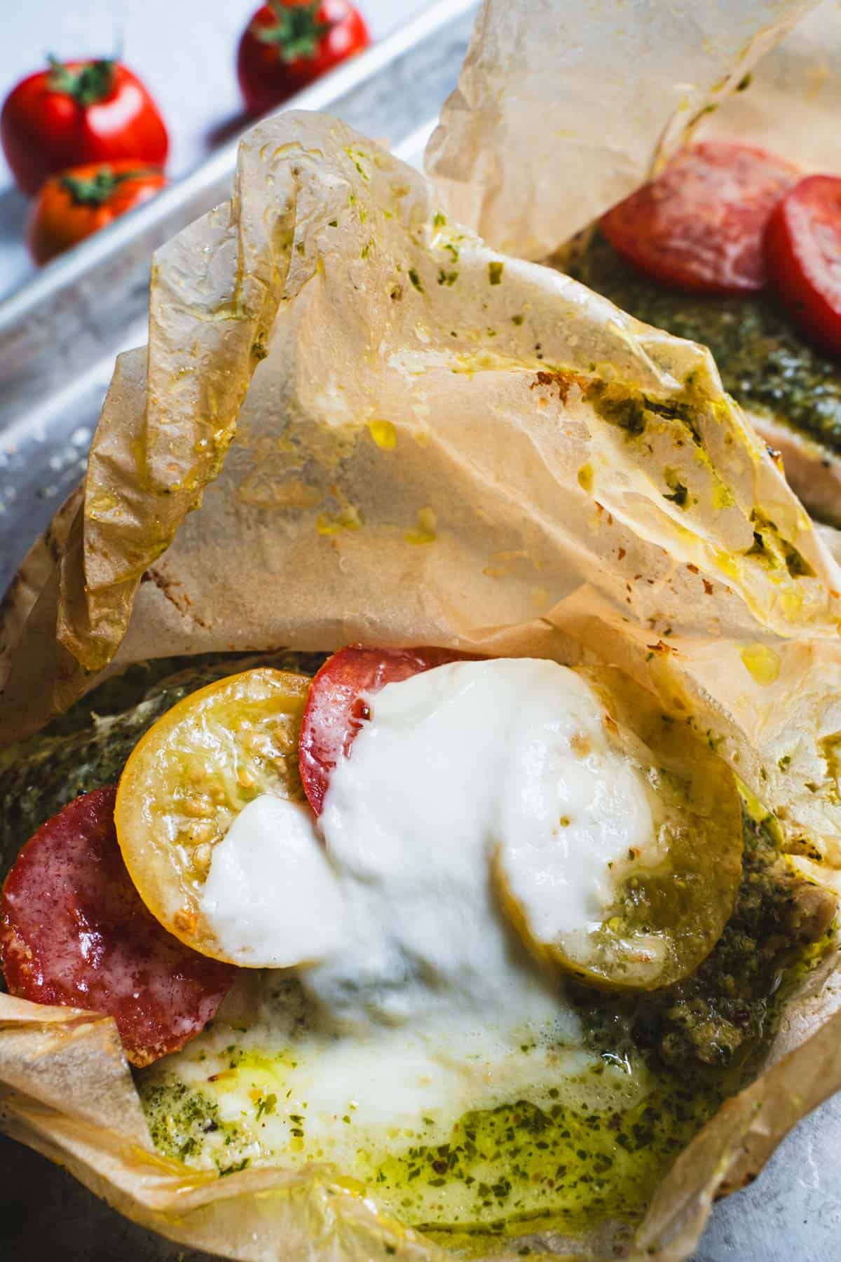 baked pesto chicken in on a baking sheet in opened parchment pouches