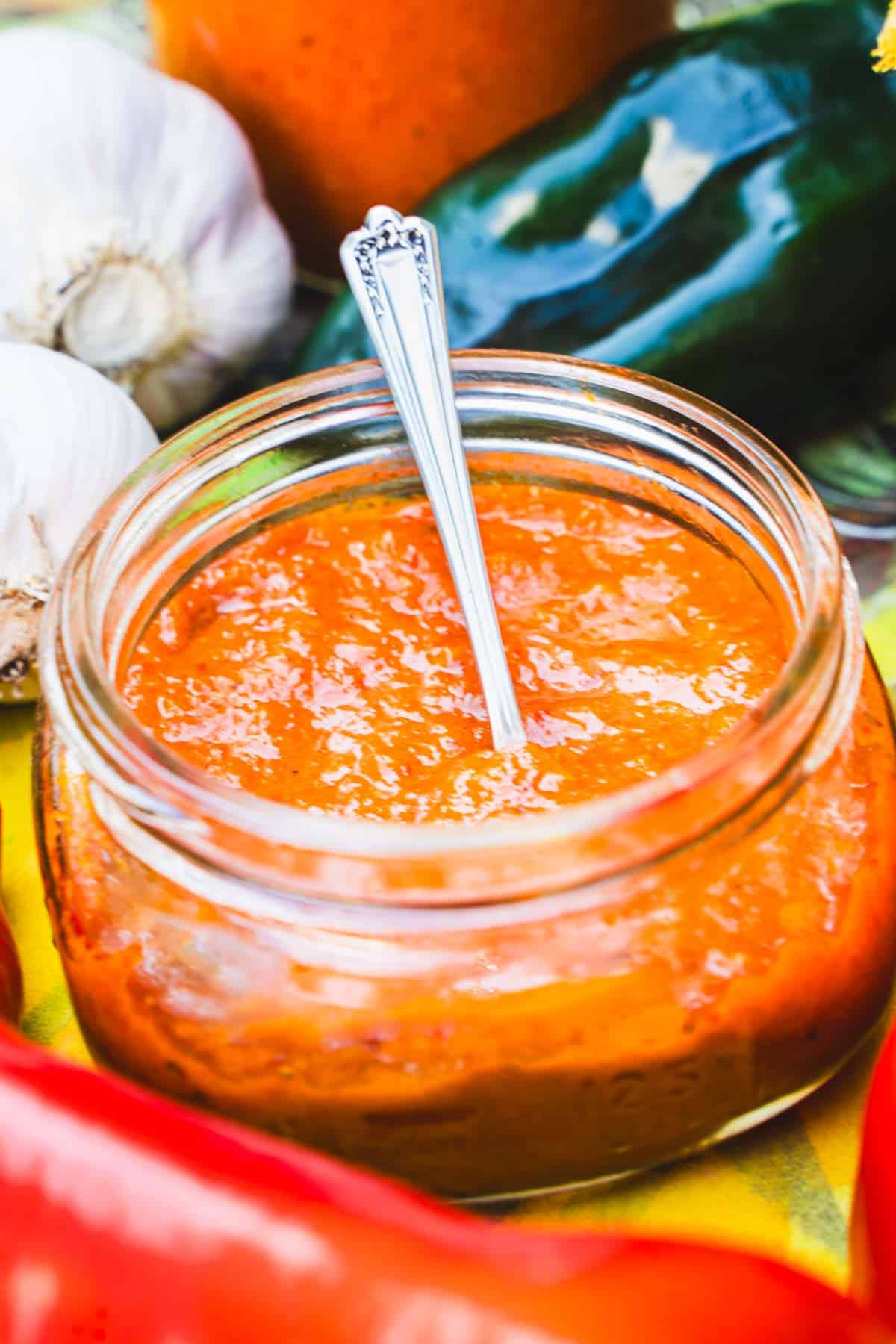 Ajvar sauce in a wide mouth 4 ounce mason jar surrounded by ajvar recipe ingredients