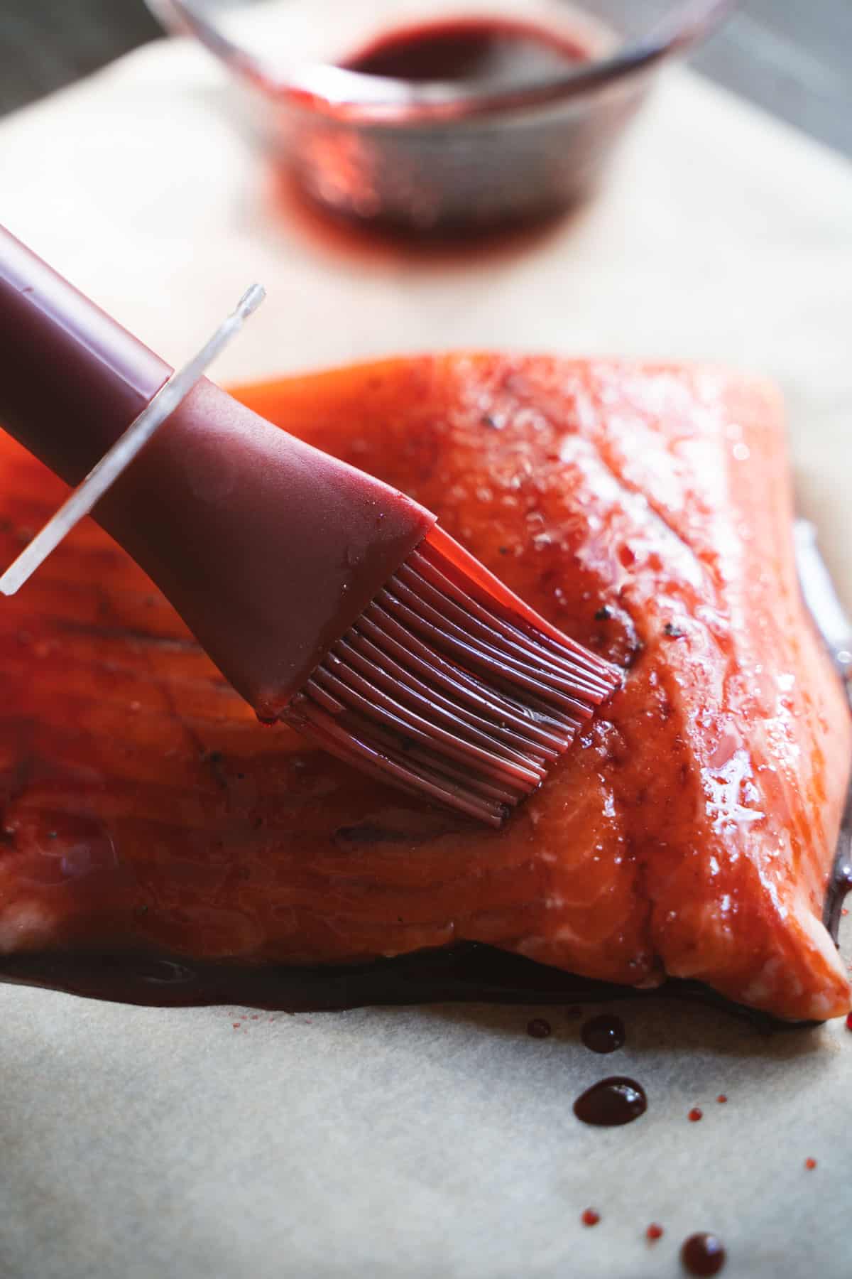 cherry glaze being applied with a basting brush to Salmon on parchment paper.