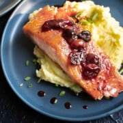 Baked salmon with cherry glaze on a blue plate served over mashed potatoes