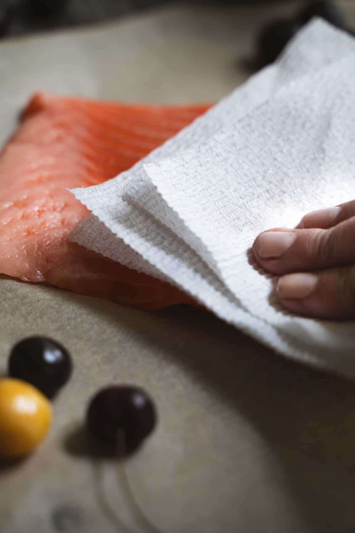 single hand patting dry salmon filet with paper towel
