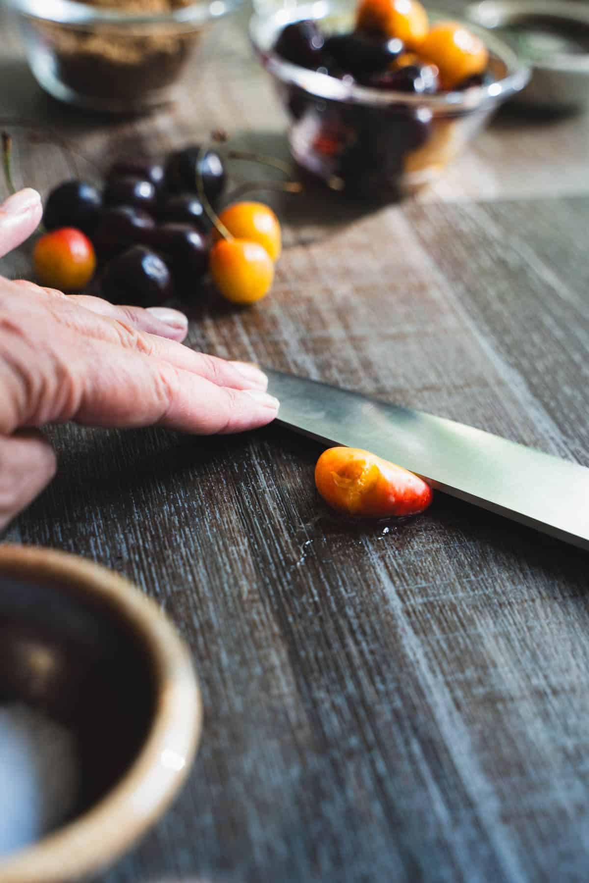 Chef's knife pressed down on a cherry smashing it with the flat edge.