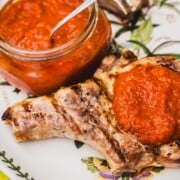 gas grilled pork chops on a white platter with ajvar dipping sauce on one chop