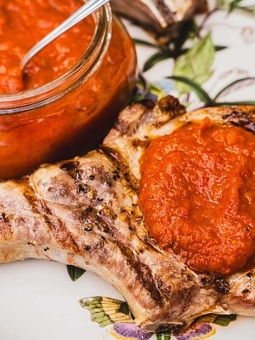 gas grilled pork chops on a white platter with ajvar dipping sauce on one chop