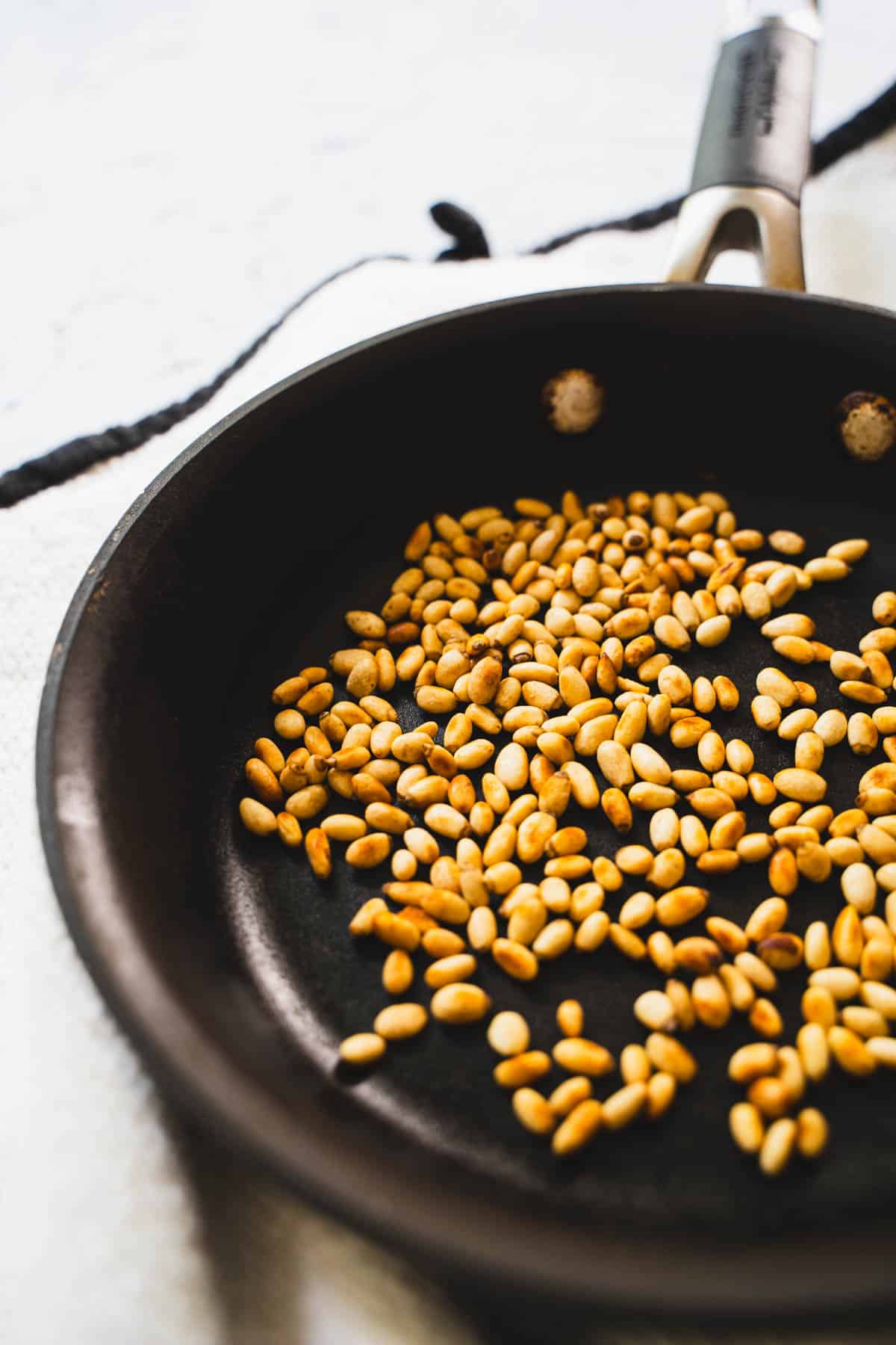 toasted pine nuts in a black small skillet on a white table