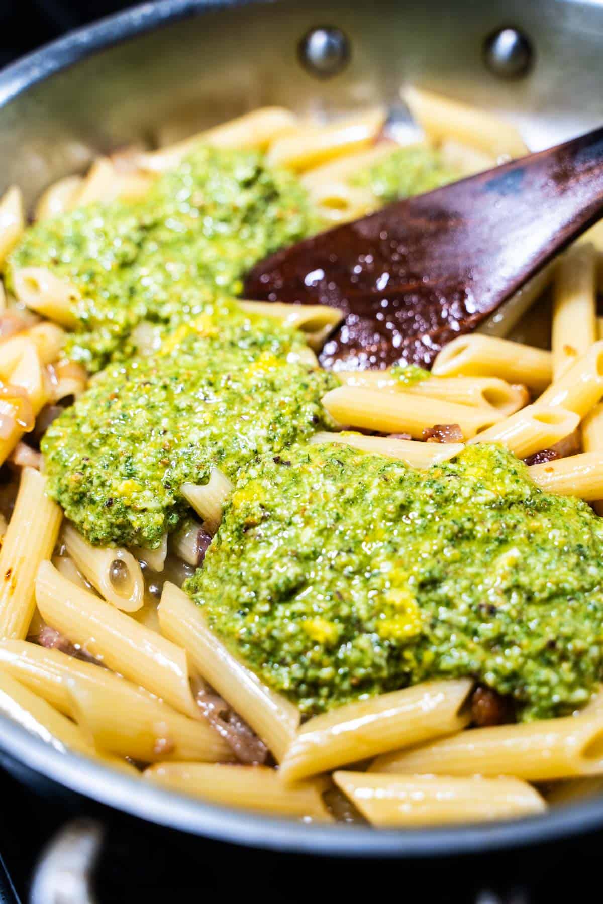 PIstachio pesto on top of penne pasta in a skillet with a wooden spoon