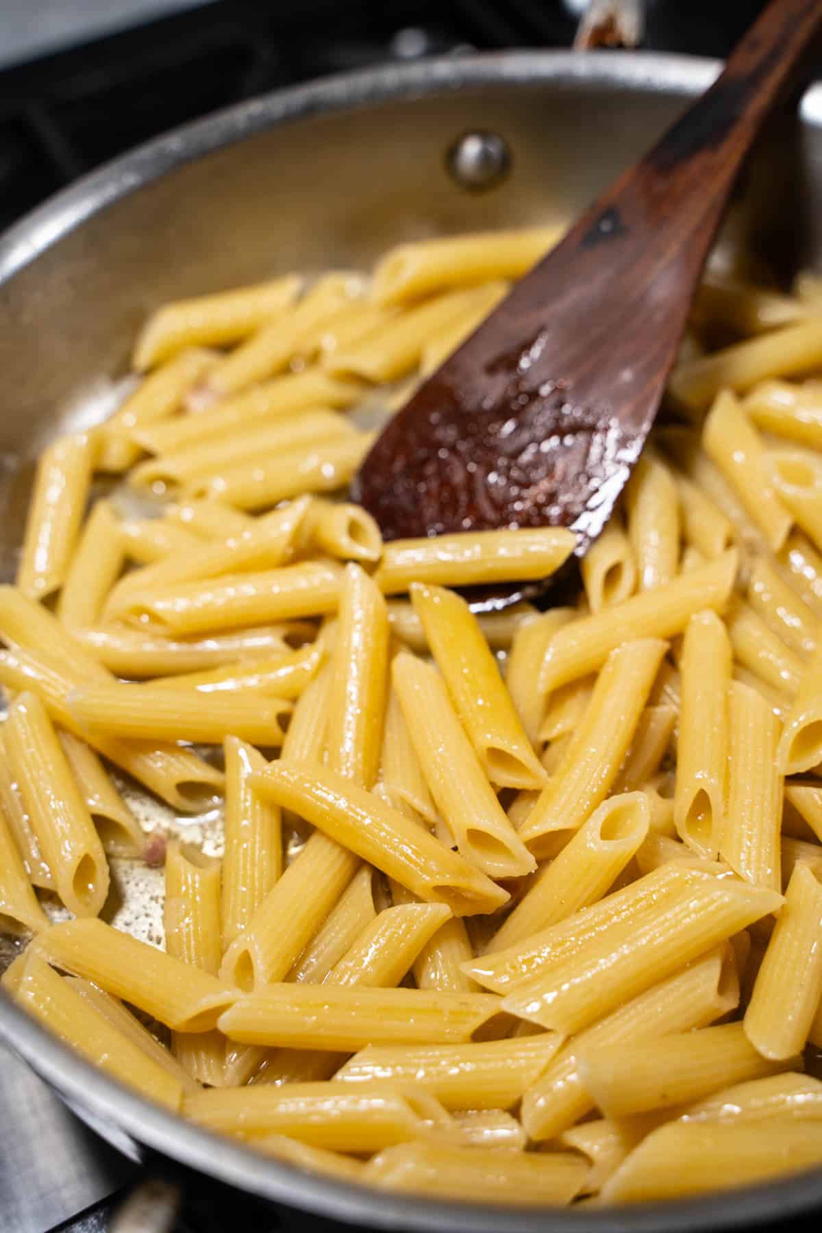 Pasta in a skillet being stirred by a wooden spoon