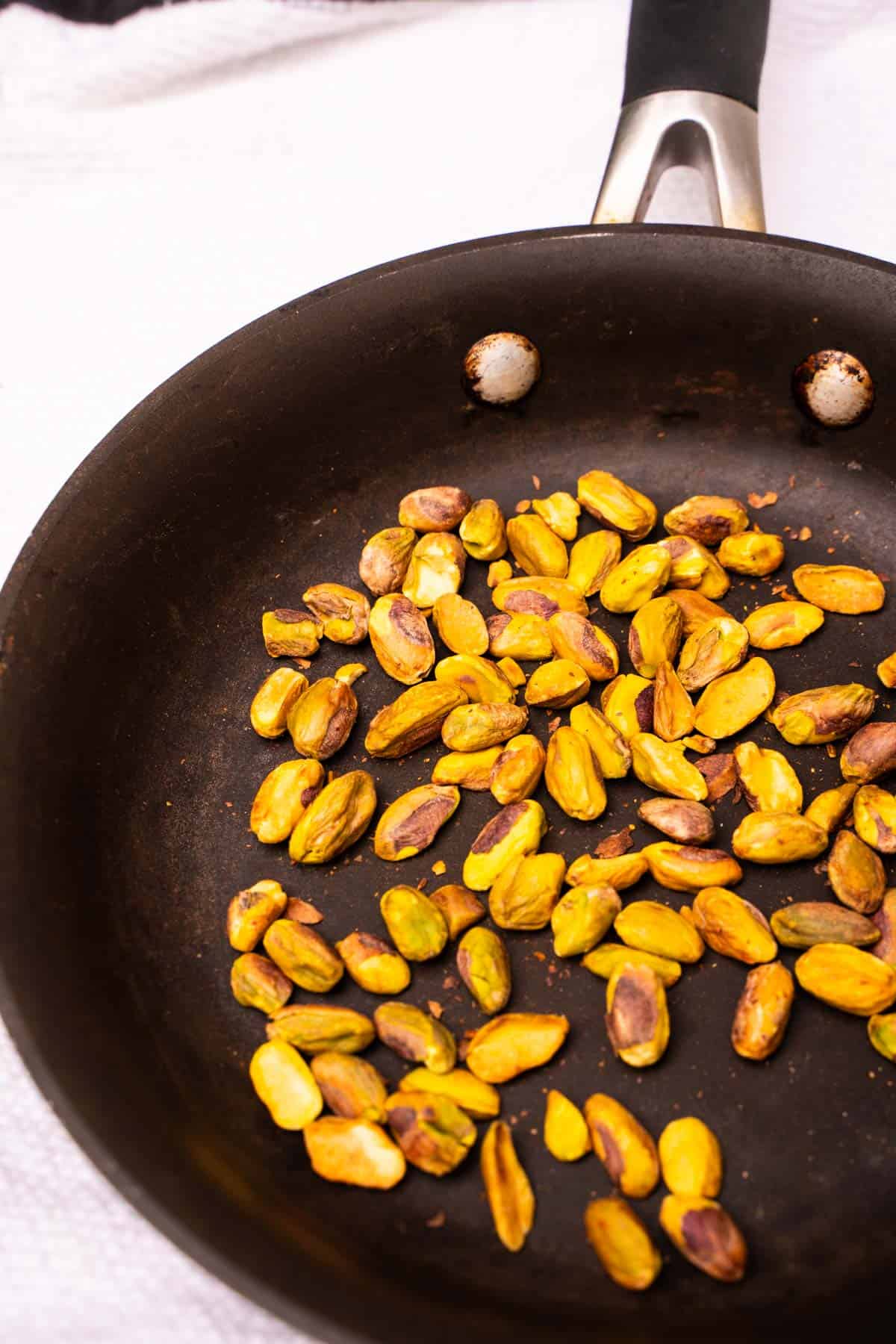 Toasted pistachios in a black skillet on a white table