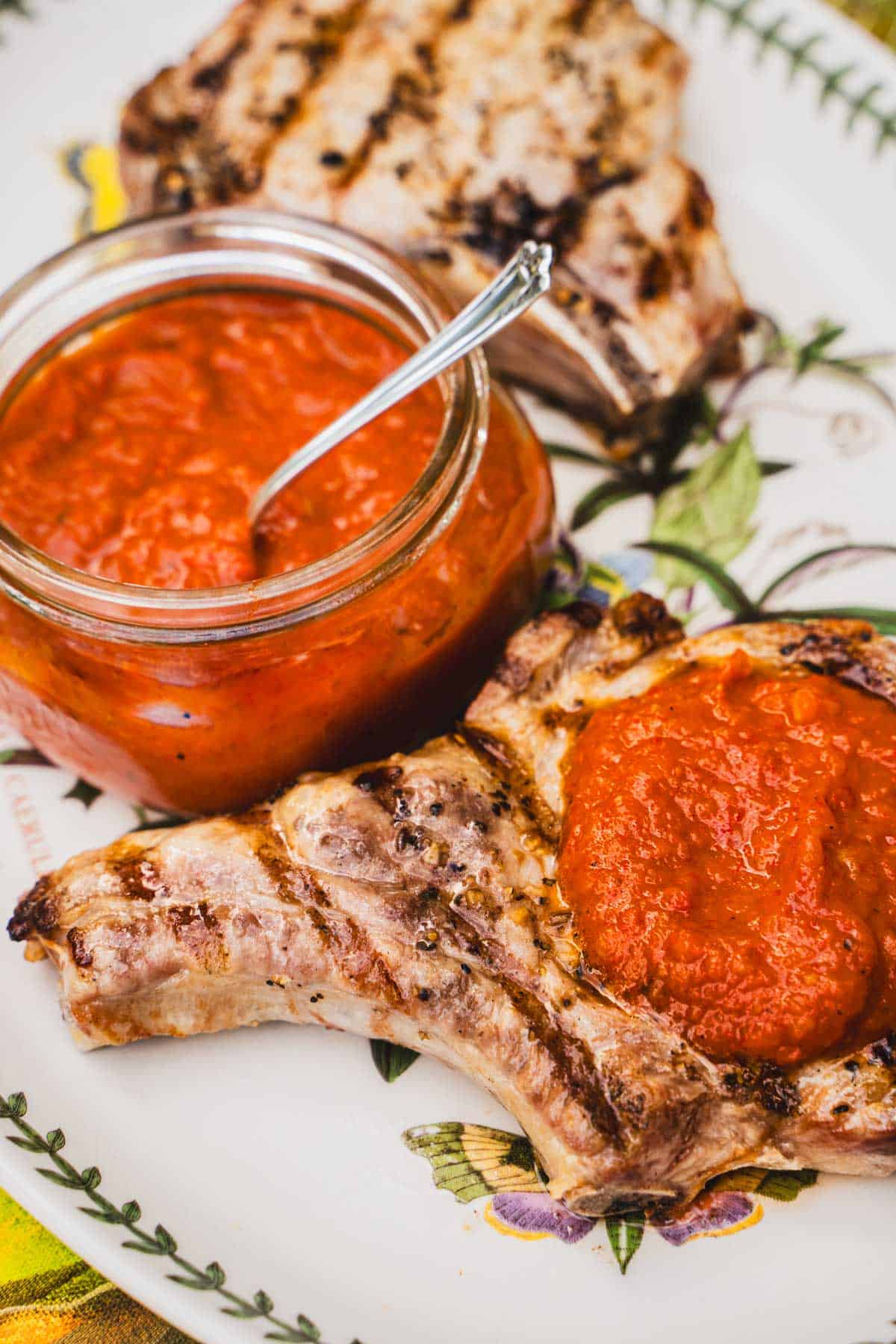 gas grilled pork chops on a white platter with ajvar dipping sauce on one chop