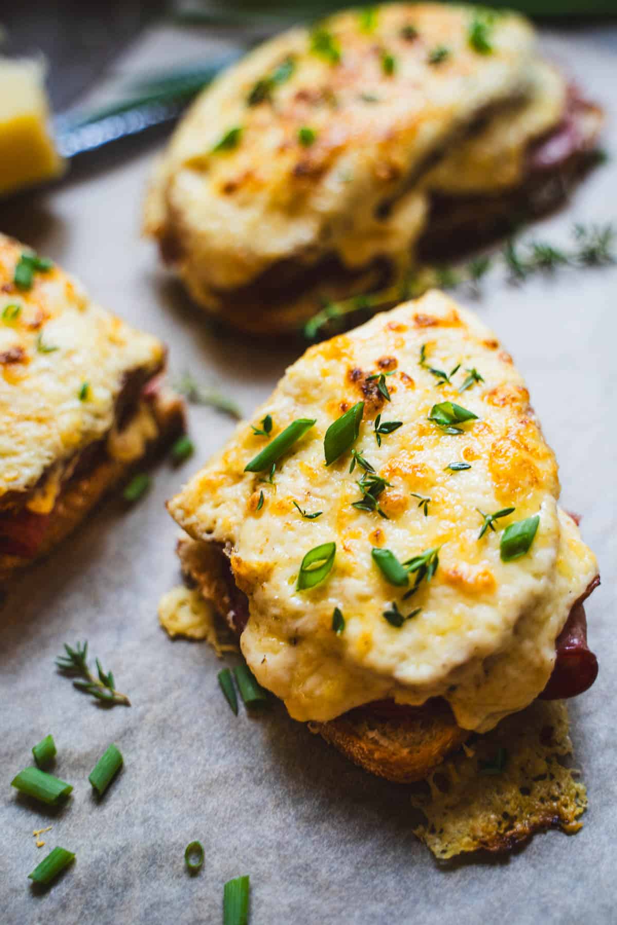 Croque Monsieur Sandwich on parchment paper cut in halves garnished with chives and thyme