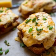 Croque Monsieur Sandwich on parchment paper cut in halves garnished with chives and thyme
