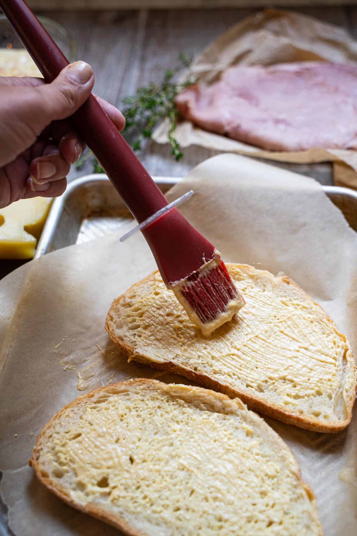 hand holding a basting brush to spread slice of bread with mustard