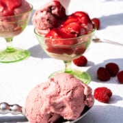 no churn Raspberry ice cream in green ice cream glass dessert cups and a clear tall ice cream glass and a scoop on a silver spoon sitting on a white table