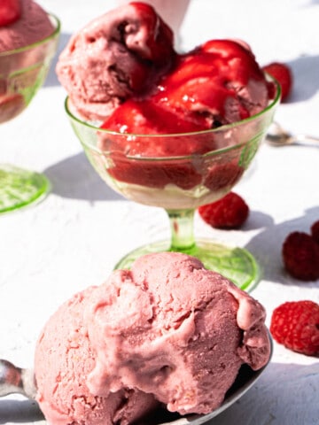 no churn Raspberry ice cream in green ice cream glass dessert cups and a clear tall ice cream glass and a scoop on a silver spoon sitting on a white table