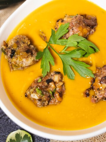 Creant Autumn Squash and Meatball Soup in a white soup bowl garnished with parsley.