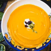 Curry Autumn Squash and Carrot Soup in a soup bowl garnished with yogurt, cranberries and pepitas.
