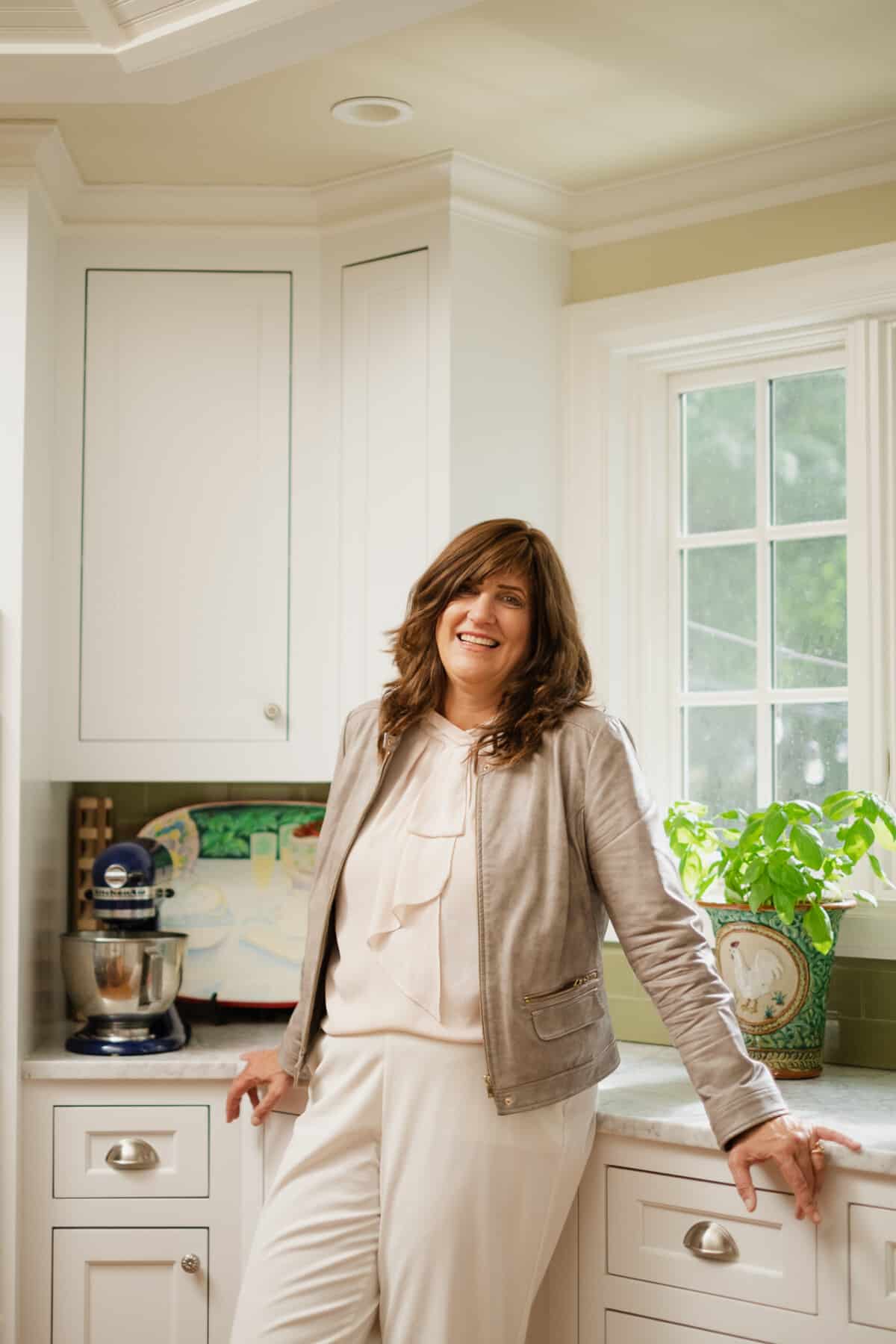 Pam Werley, founder of our table 4 2 standing in the kitchen leaning against counter.