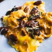Pumpkin sauce for pasta tossed with cheese ravioli with crispy fried sage leaves and toasted pecans on the top served on a blue plate.
