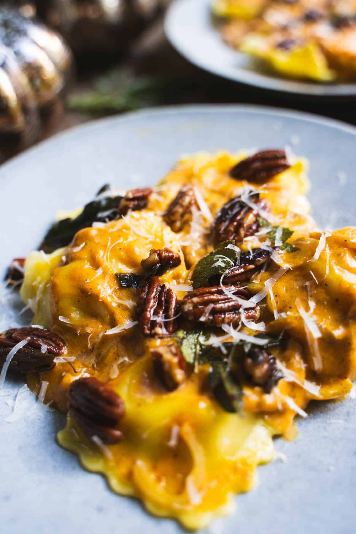 Pumpkin sauce for pasta tossed with cheese ravioli with crispy fried sage leaves and toasted pecans on the top served on a blue plate.