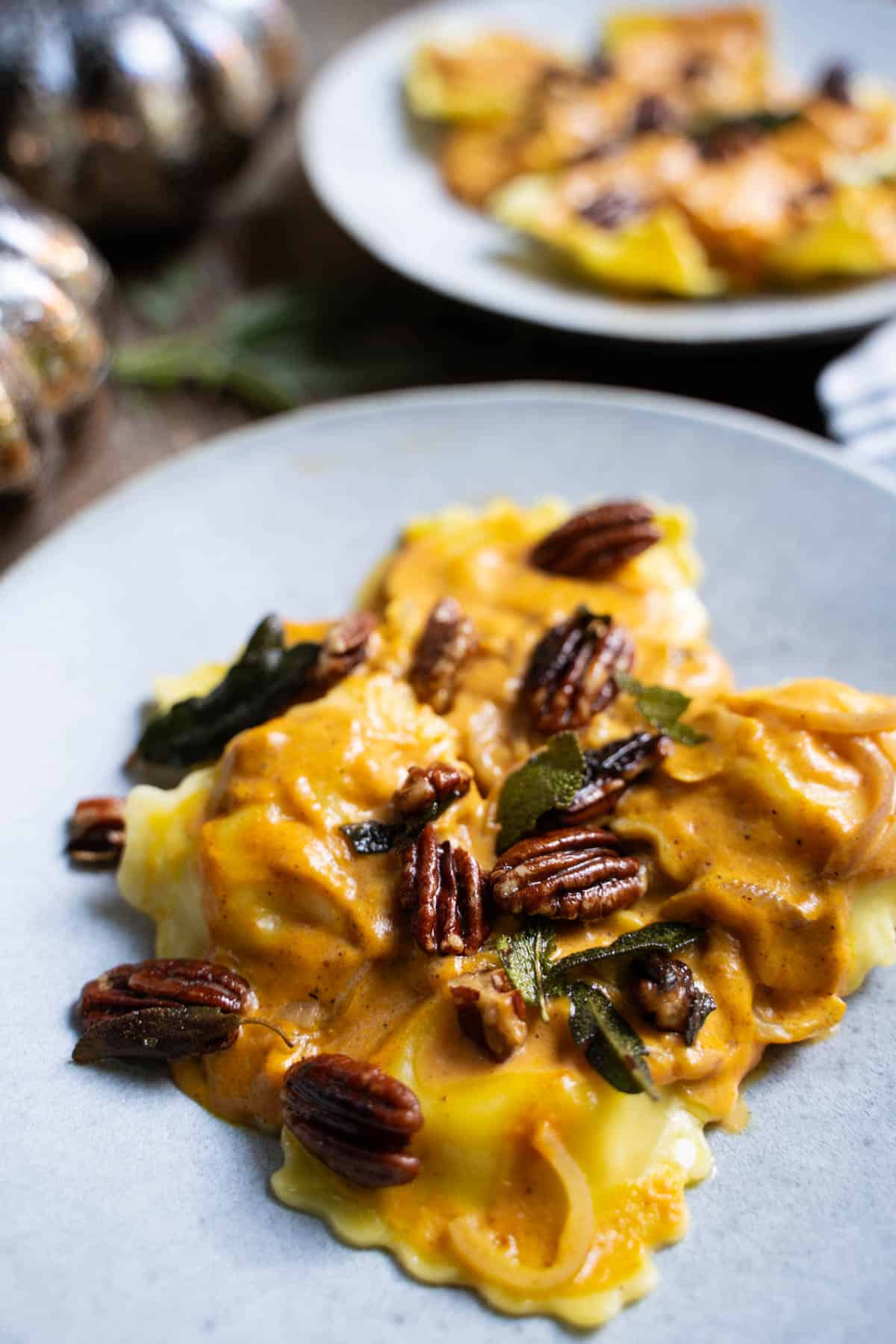 Pumpkin sauce for pasta over cheese ravioli sprinkled with fried sage leaves and nuts on 2 blue dinner plates